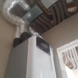 Rekuperator Zehnder w folii ochronnej, podłączony do systemu wentylacji z rurami spiro i kanałami w suficie podwieszanym.