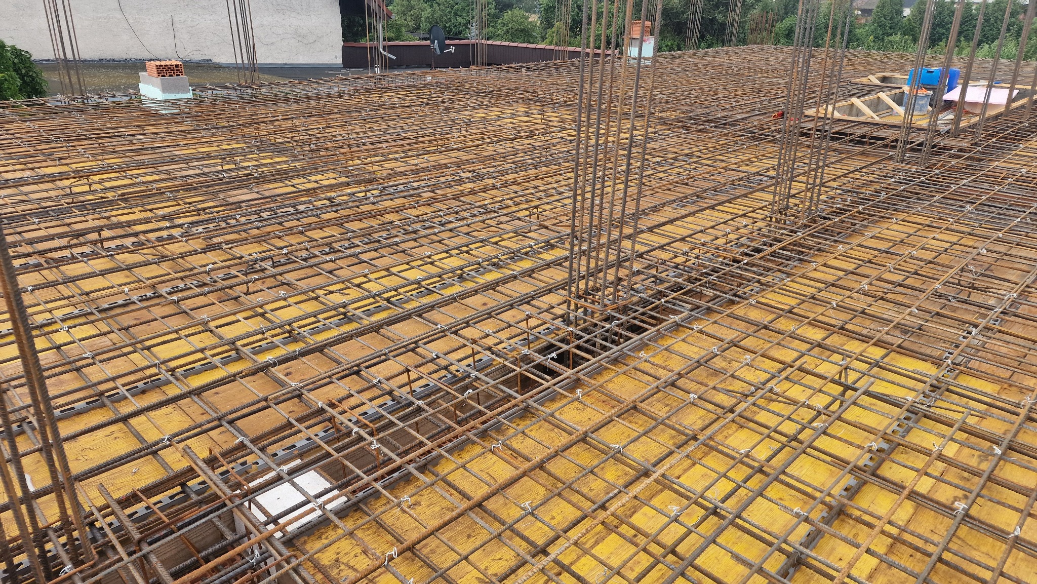 Zbrojenie stropu na żółtym szalunku, widoczne pionowe pręty zbrojeniowe oraz elementy drewniane szalunku w tle.
