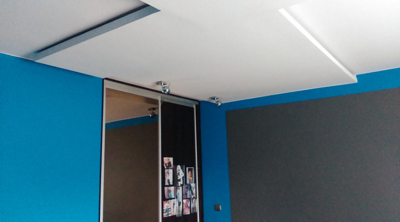 Błękitna ściana, biały sufit z oświetleniem punktowym i szafa przesuwna z lustrem, na której umieszczono zdjęcia. Kontrastowe kolory ścian.