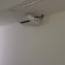 Zamontowany projektor multimedialny marki Epson na białej ścianie w biurze, widoczne kable i uchwyt montażowy.