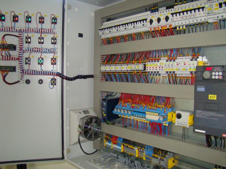 Otwarta szafa sterownicza z licznymi przewodami, bezpiecznikami i elementami elektrycznymi. Widoczny wentylator chłodzący oraz oznaczenia A07 na urządzeniu.