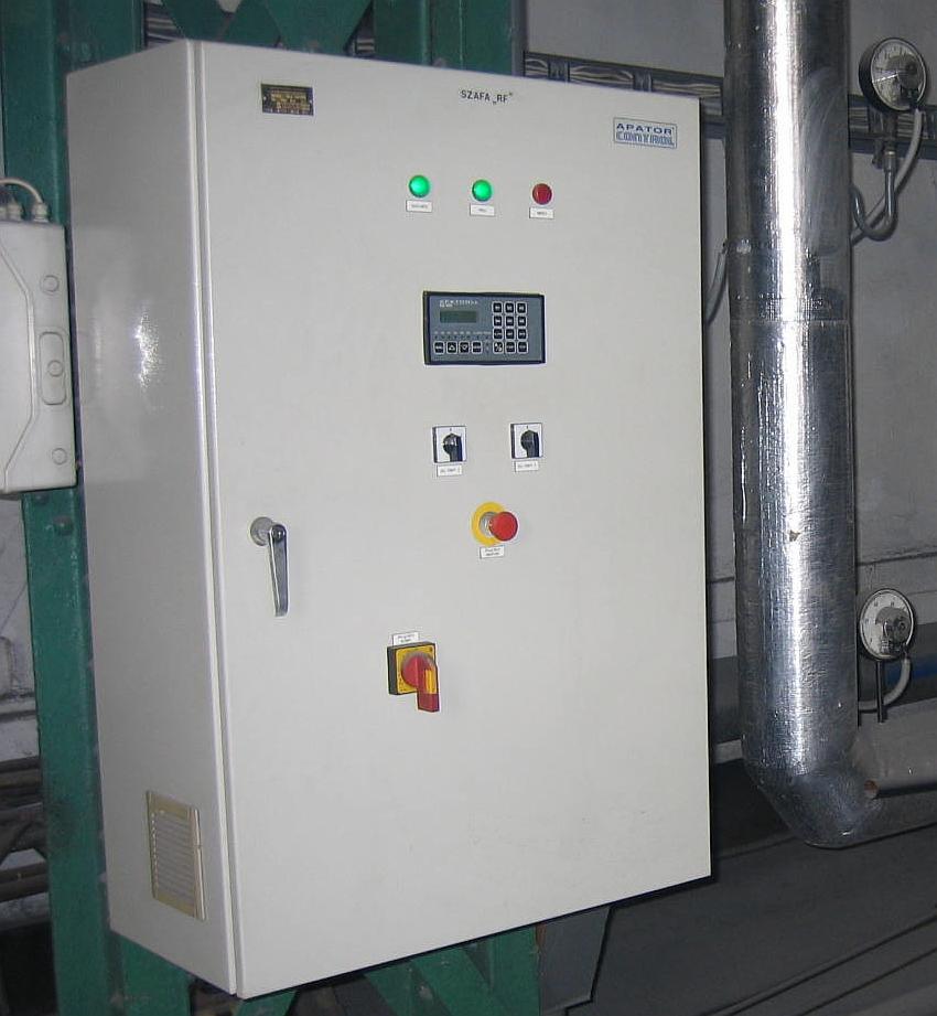Biała szafa sterownicza 'SZAFA RF' z zielonymi i czerwonymi lampkami, wyświetlaczem, przełącznikami i awaryjnym wyłącznikiem, obok rura instalacyjna.