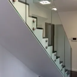 Szklana balustrada schodowa z mocowaniami punktowymi, widoczne miseczki dla zwierząt na czarnej podłodze.