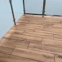 Balkon wyłożony płytkami imitującymi drewno, z balustradą ze szkła mlecznego i stali nierdzewnej, widok z góry pod kątem, ślady fugi na płytkach.