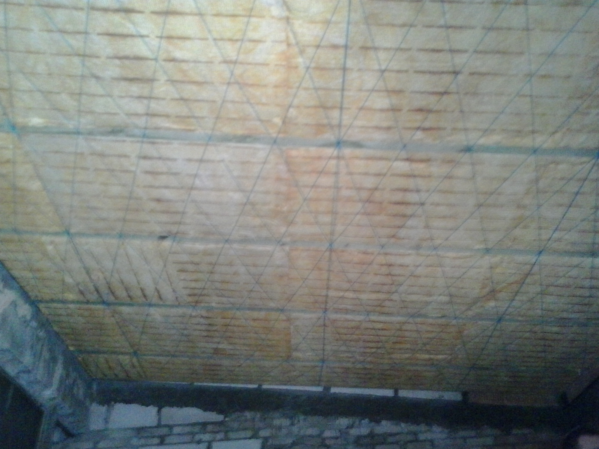 Montaż izolacji na suficie z widoczną siatką wzmacniającą i surową ścianą w tle.