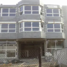 Surowy budynek w trakcie budowy z zamontowanymi oknami PCV z białymi ramami, widoczne rusztowania i materiały budowlane.