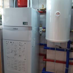 EKO 2020 Franciszek Raciborski - Biała pompa ciepła Vaillant z czerwonym zbiornikiem wyrównawczym i białym zasobnikiem ciepłej wody, podłączona do instalacji z rurami w kolorze niebieskim i czerwonym, zamontowana w pomieszczeniu...