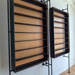 ALU-STAL - Dwie metalowe, czarne półki z perforowanym złotym tłem, zamontowane na ścianie. Minimalistyczny design z oświetleniem LED. Widoczny fragment podłogi z parkietem.