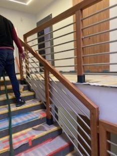 Nowoczesne schody wewnętrzne z drewnianymi poręczami i metalowymi balustradami, zabezpieczone folią malarską podczas prac wykończeniowych.