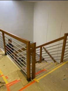 Wewnętrzne schody z drewnianymi słupkami i poziomymi, metalowymi prętami balustrady, zabezpieczone kartonem na czas remontu, widok z góry.