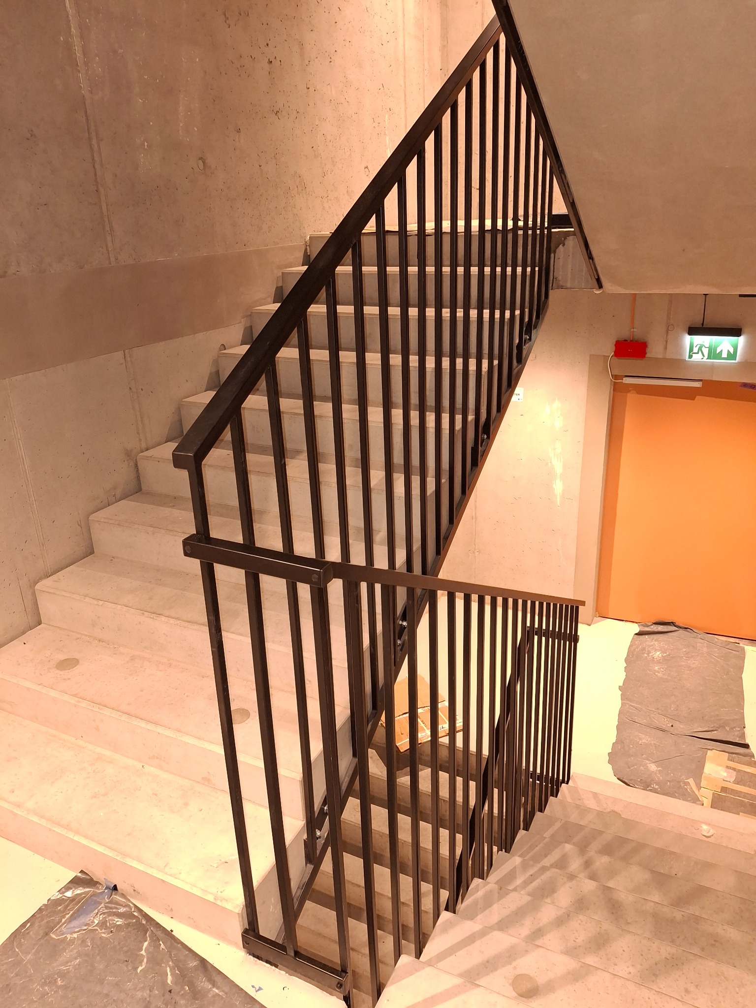 Nowoczesne schody z metalową balustradą w Wągrowcu. Minimalistyczny design, betonowe ściany, widoczne zabezpieczenia podłogi. Solidne wykonanie.