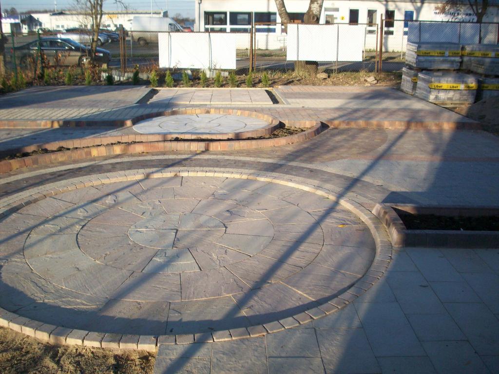 Wzory z kostki brukowej: okrągły plac z szarej kostki, obrzeża z cegły, różne faktury i odcienie szarości. Ekspozycja na zewnątrz w słoneczny dzień.