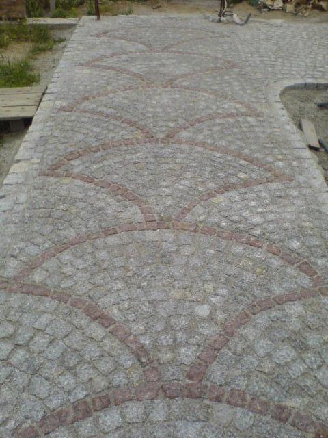 Granitowa ścieżka z dekoracyjnym wzorem wachlarza z czerwonej kostki, ukazana z perspektywy chodnika. Szare kostki tworzą tło dla wzoru.