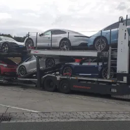 Laweta w Dynowie przewozi osiem luksusowych samochodów Porsche w różnych kolorach, ułożonych na dwóch poziomach, z widocznym logo firmy transportowej Transhad na kabinie.