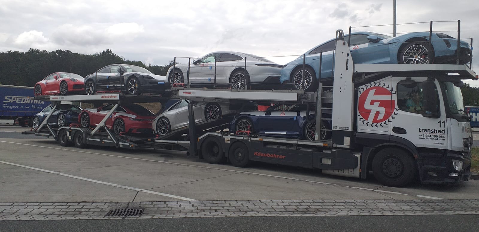 Laweta w Dynowie przewozi osiem luksusowych samochodów Porsche w różnych kolorach, ułożonych na dwóch poziomach, z widocznym logo firmy transportowej Transhad na kabinie.