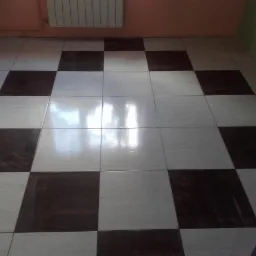 Ułożona szachownica z brązowo-białych, błyszczących płytek podłogowych w pomieszczeniu z grzejnikiem na ścianie.