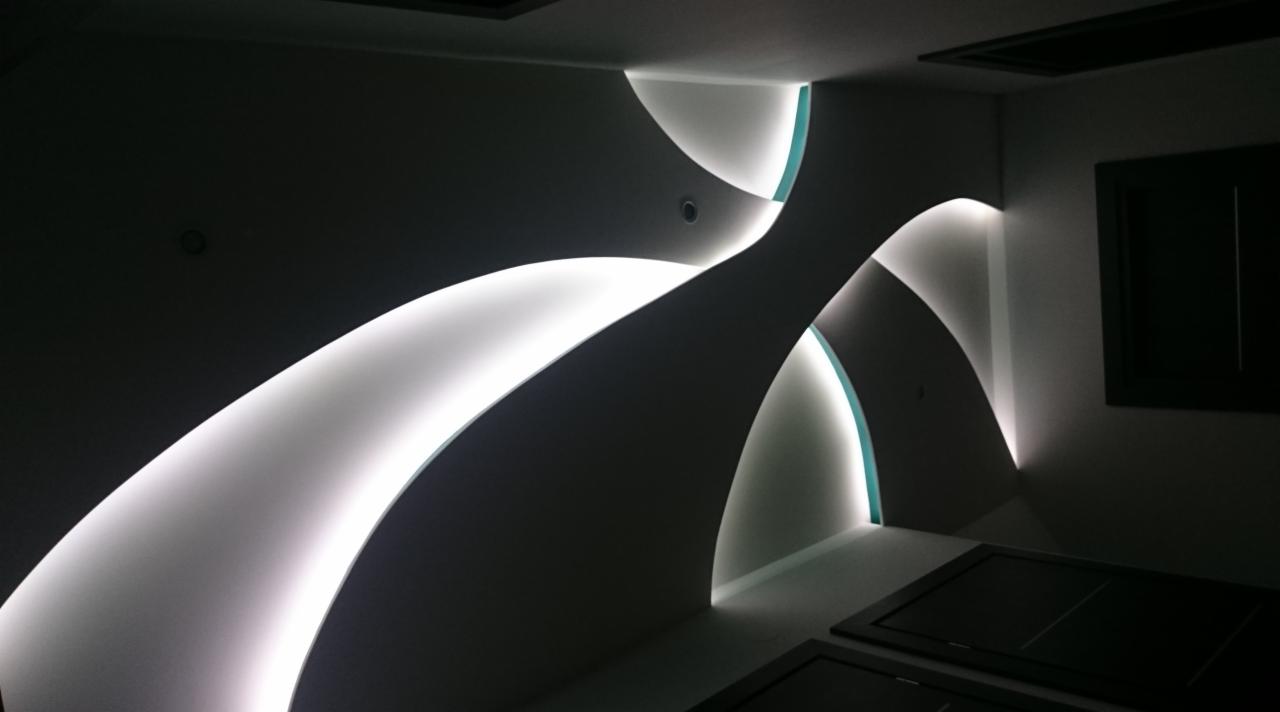 Nowoczesne wykończenie sufitu z oświetleniem LED w kształcie łuków. Białe ściany, ciemne elementy wyposażenia.  Minimalistyczny design z akcentami światła.