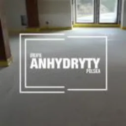 Gładka, jasnoszara wylewka anhydrytowa, świeżo wykonana we Wrocławiu. Widoczne taśmy zabezpieczające przy ścianach i oknach. Minimalistyczne wnętrze w trakcie wykańczania.