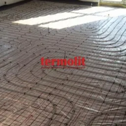 Rozłożone rury ogrzewania podłogowego na siatce z folii, widoczne logo producenta Termolit, przygotowane do zalania wylewką.