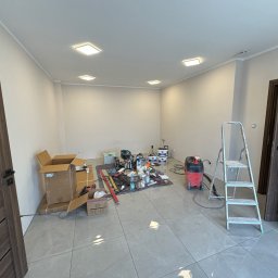 Remont pokoju w Ostravie: widok na przygotowane pomieszczenie z narzędziami, drabiną i materiałami malarskimi. Podłoga wyłożona szarą płytką, ściany przygotowane do malowania.