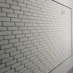 Ściana wykończona białymi cegłami dekoracyjnymi z czarną ramą, widoczne kable elektryczne w górnym rogu.
