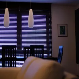 Salon z ciemnymi żaluzjami poziomymi, białymi lampami wiszącymi i fragmentem jasnej sofy na pierwszym planie.