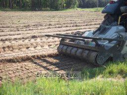 Ciągnik z mulczerem w trakcie pracy na polu, widoczne świeżo zmielone resztki roślinne i ślady opon, w tle las.