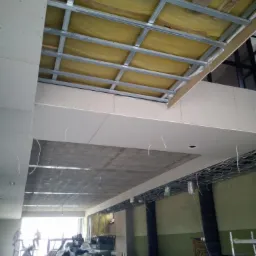 Montaż sufitu podwieszanego z metalową konstrukcją i żółtą izolacją w budynku w Soborzycach, widoczne przewody elektryczne i materiały budowlane.