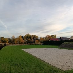 Manufaktura Zieleni - Przygotowany teren pod przyszły ogród z piaskowym podłożem, świeżo skoszonym trawnikiem i ogrodzeniem panelowym w tle, częściowo widoczne domy jednorodzinne.