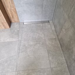 GUS ER-House Rafał Siwiec - Szare, matowe płytki podłogowe i ścienne w łazience z odpływem liniowym, widok z góry.