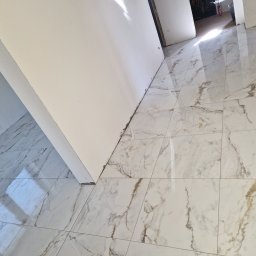 GUS ER-House Rafał Siwiec - Błyszcząca, marmurowa podłoga w odcieniach bieli i beżu, świeżo ułożona w jasnym pomieszczeniu, z fragmentem białej ściany i widocznym progiem drzwi.
