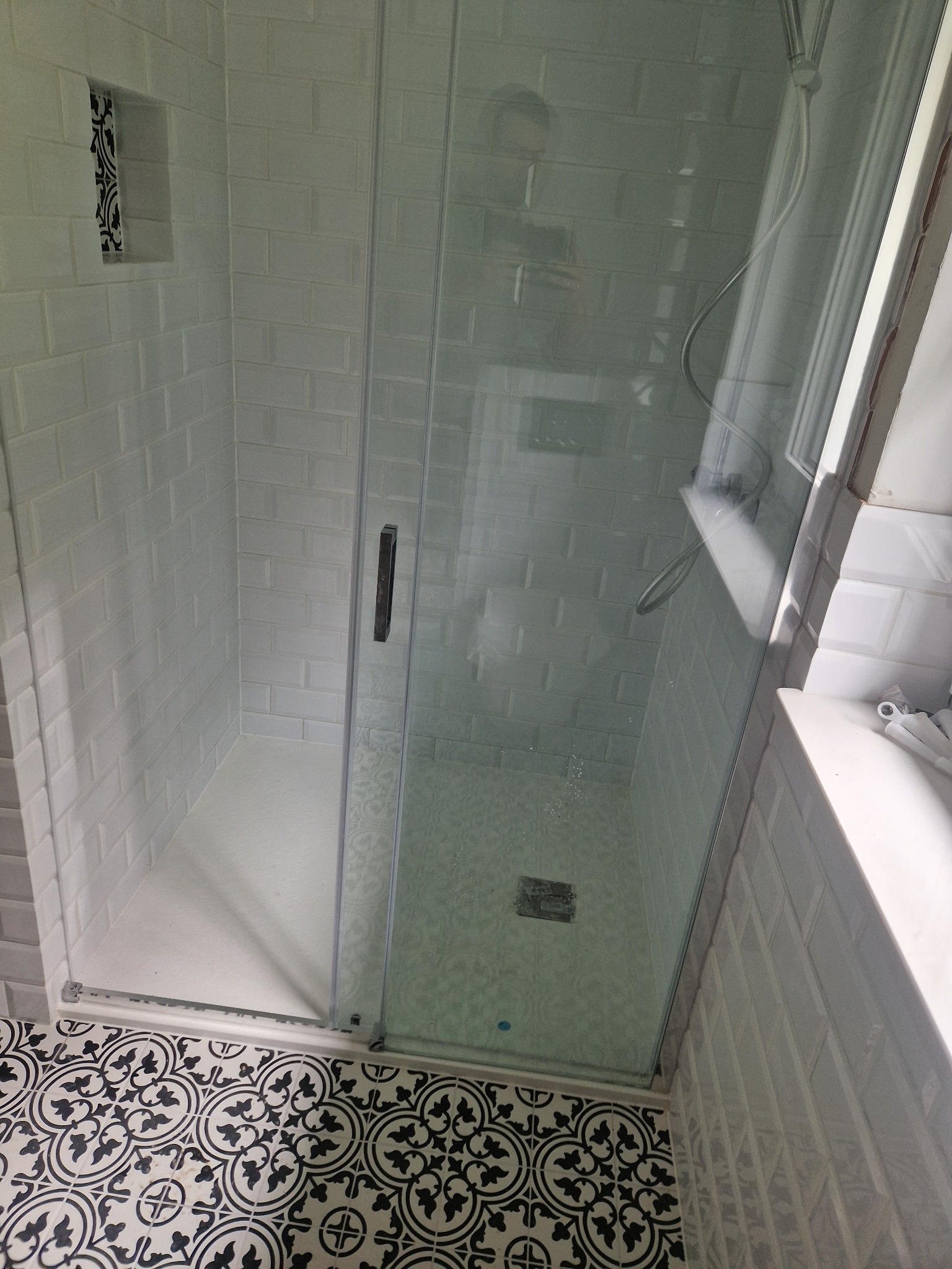 Biała kabina prysznicowa z deszczownicą, wyłożona kafelkami typu cegiełka i z wzorzystą podłogą. W ścianie wnęka z dekoracyjnymi płytkami. Widoczne detale wykończenia.