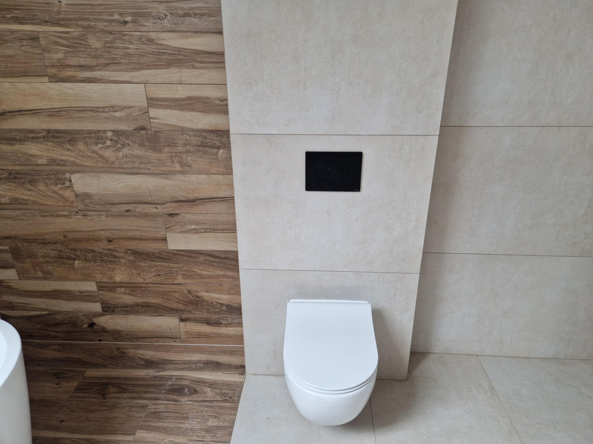 Nowoczesna toaleta podwieszana z czarnym panelem spłukującym, otoczona płytkami imitującymi drewno i beżowym gresem. Minimalistyczny design łazienki.