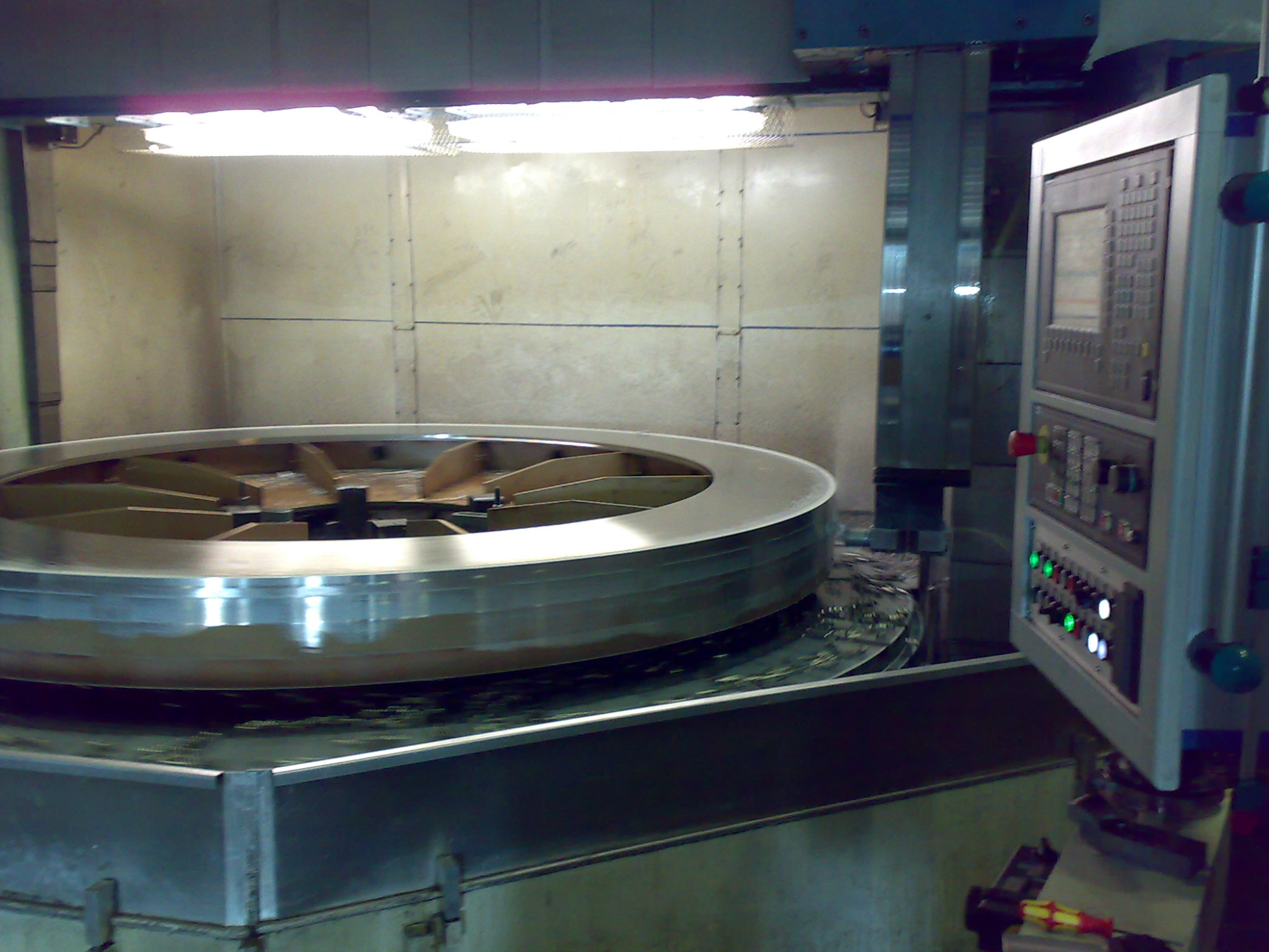 Obrabiany metalowy pierścień wewnątrz maszyny CNC z widocznym panelem sterowania i oświetleniem roboczym.