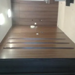 Drewniane schody z ukrytym oświetleniem w listwach, prowadzące na górę, z zabudową ścienną z paneli drewnianych i ukrytymi drzwiami.