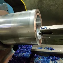 Metalowy element obrabiany na tokarce, wióry w kolorze niebieskim. Widoczne narzędzie skrawające i obracający się przedmiot.