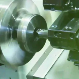 Dynamiczne ujęcie procesu obróbki metalu na tokarce CNC. Widać obracający się element i narzędzie skrawające w akcji, z logotypem firmy w prawym dolnym rogu.