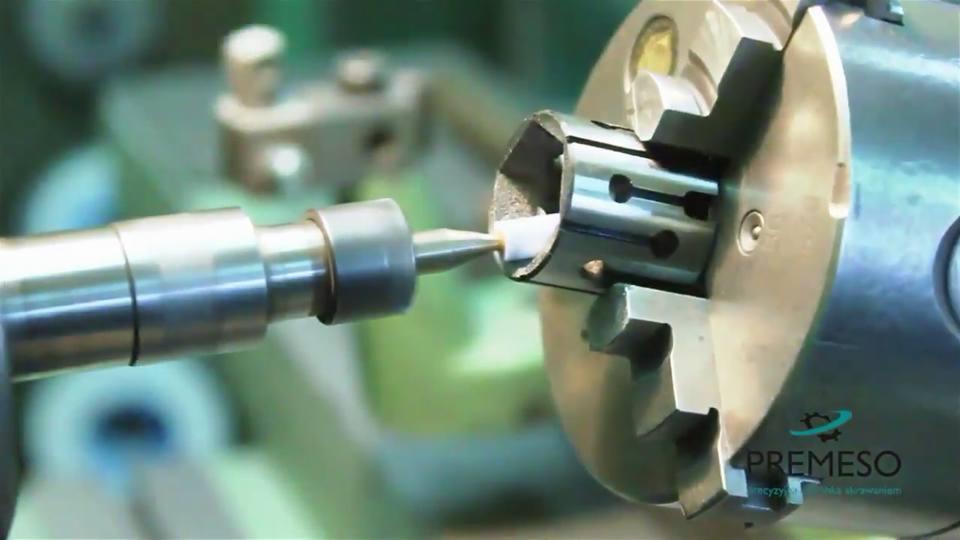 Precyzyjna obróbka metalu na tokarce CNC. Wiertło w trakcie pracy nad metalowym elementem z otworami. Widoczne logo firmy Premeso.