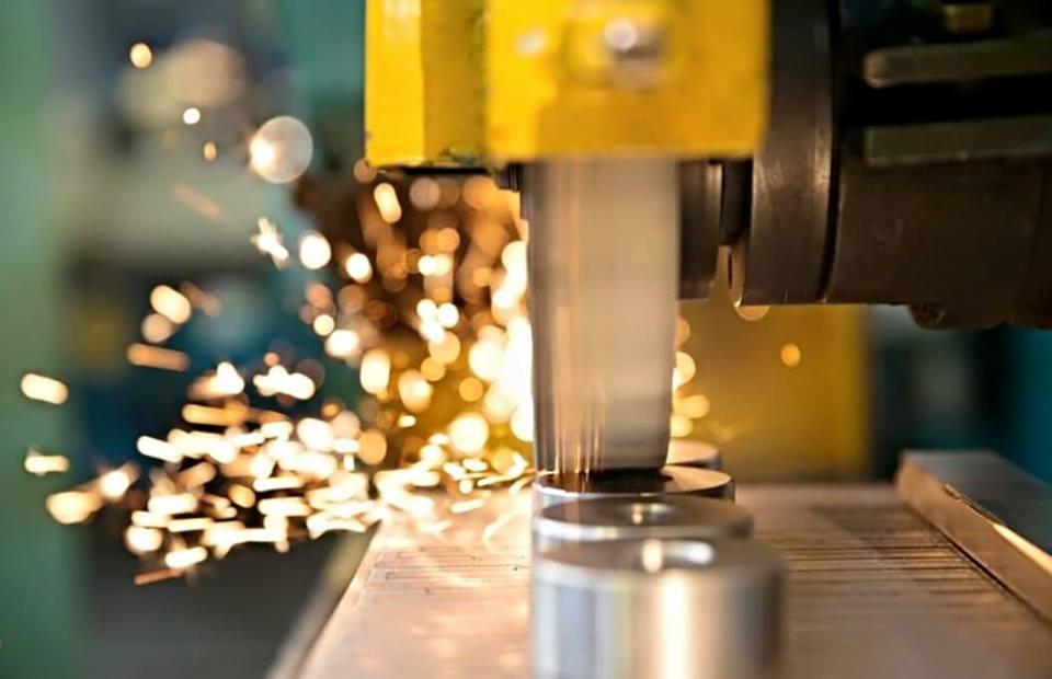 Szlifowanie metalowych elementów z iskrami, widoczna żółta maszyna i obrabiane detale. Detal w trakcie procesu obróbki.