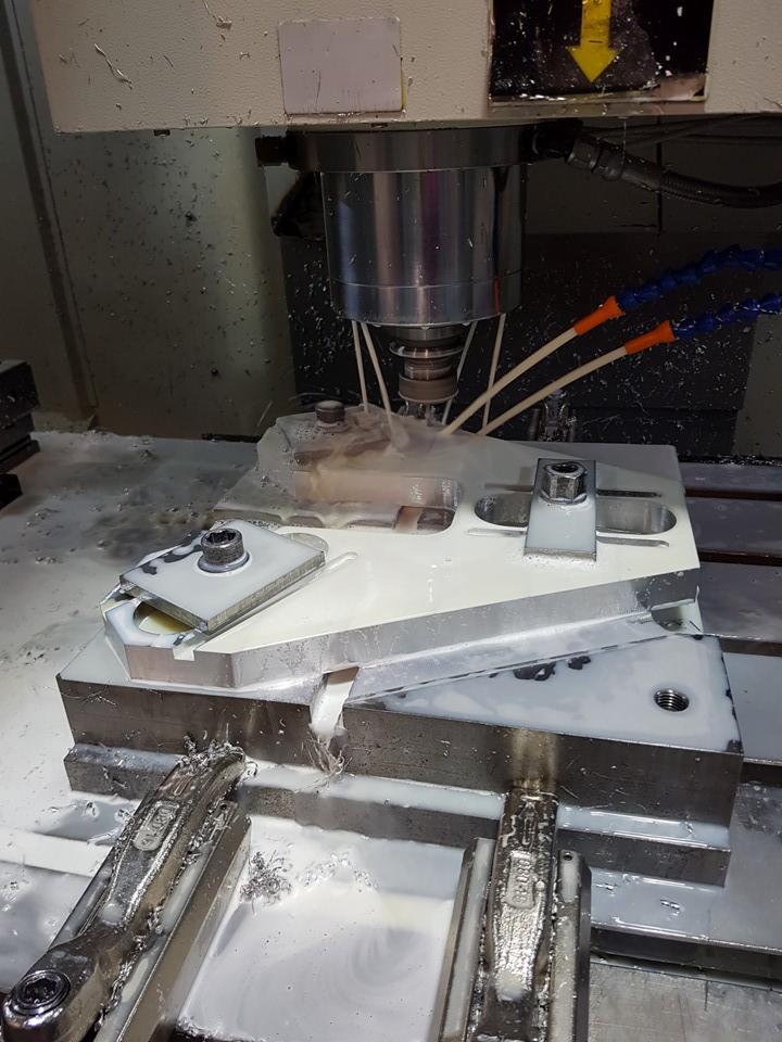 Obróbka metalu na frezarce CNC z chłodziwem. Wióry i narzędzia widoczne, obrabiany element zamocowany w uchwycie. Detal w trakcie frezowania.