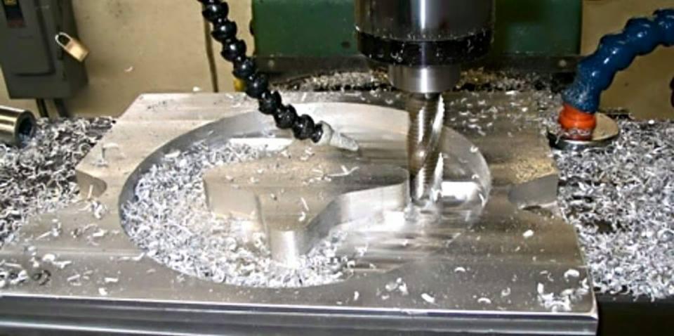 Frezarka CNC w trakcie obróbki metalu, wióry na powierzchni. Widoczny frez, uchwyt narzędziowy i chłodziwo.