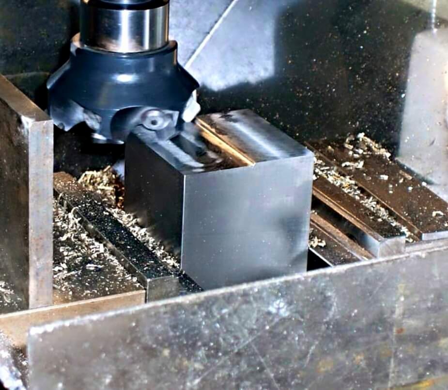 Frezowanie metalowego sześcianu frezem trzpieniowym na obrabiarce. Wióry na stole roboczym. Precyzyjna obróbka skrawaniem.