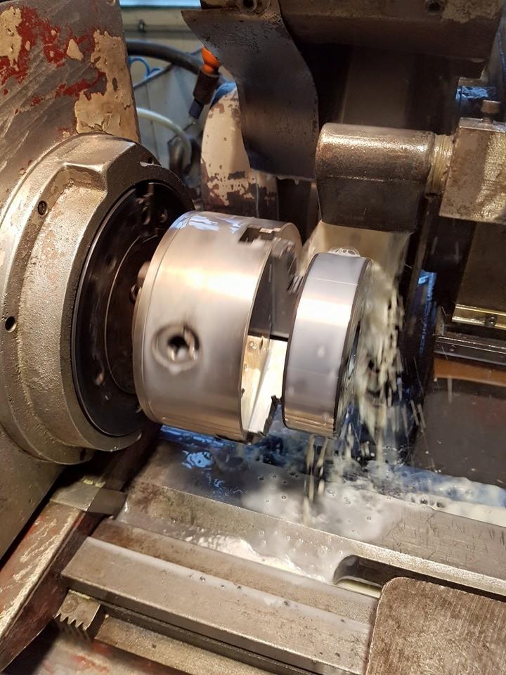 Precyzyjna obróbka metalu na tokarce z chłodzeniem, widoczne opiłki i ciecz chłodząca. Detal w trakcie toczenia, uchwyt tokarski i narzędzie skrawające w zbliżeniu.