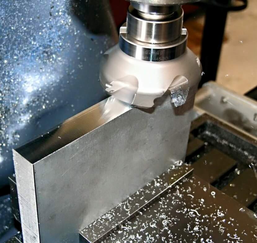 Frezer CNC w trakcie obróbki metalowego bloku, widoczne wióry i chłodziwo. Precyzyjna praca na maszynie CNC.