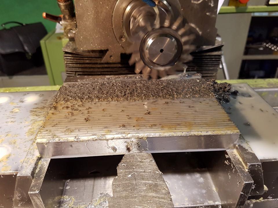 Frezarka CNC w trakcie pracy, wióry metalowe na obrabianym elemencie. Widoczny frez i chłodziwo. Obróbka rowków w metalowym bloku.