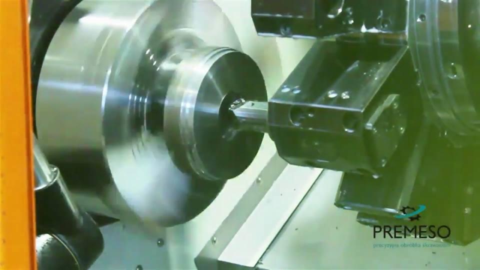 Dynamiczne ujęcie procesu obróbki metalu na tokarce CNC. Widać obracający się element i narzędzie skrawające w akcji, z logotypem firmy w prawym dolnym rogu.
