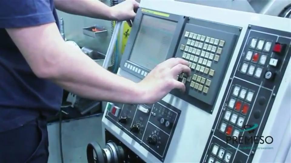 Operator wprowadza dane do panelu sterowania maszyny CNC. Widoczne przyciski, ekran i dłoń osoby obsługującej urządzenie.