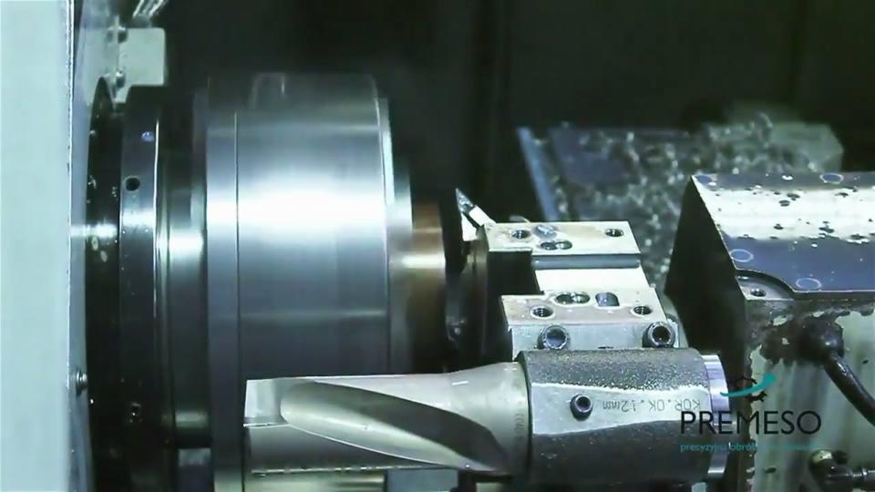 Metalowy element obrabiany na tokarce CNC z użyciem wiertła. W tle widoczny fragment maszyny. Obróbka precyzyjna.