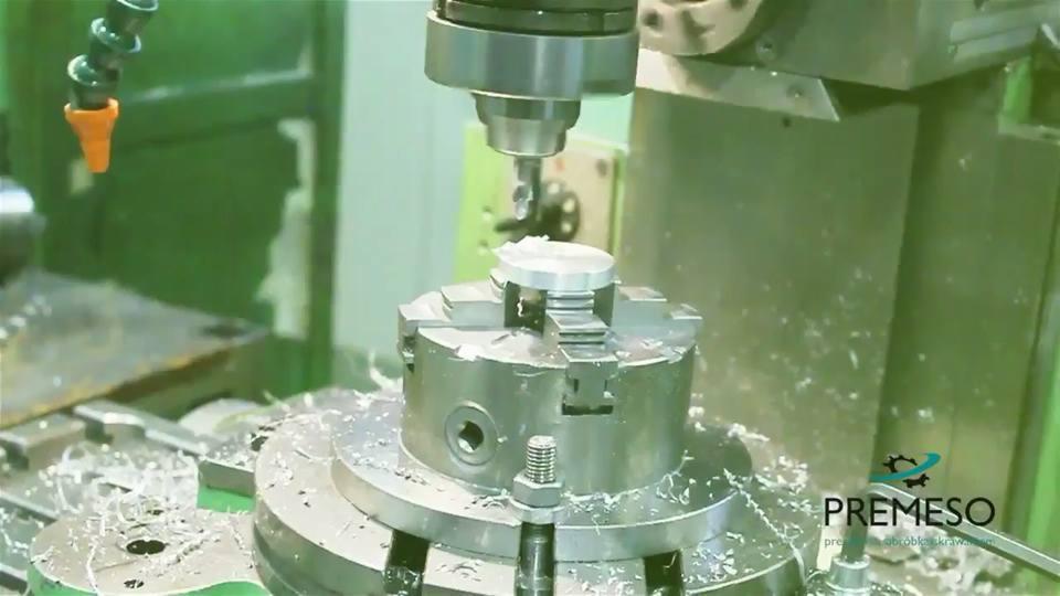 Precyzyjna obróbka metalu na obrabiarce CNC. Wióry metalowe wokół obrabianego elementu. Widoczne detale maszyny i logo firmy Premeso.