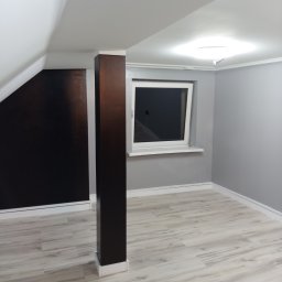 PHU Franko - Pomalowane na szaro wnętrze poddasza z oknem, drewnianą kolumną i panelami podłogowymi imitującymi drewno.